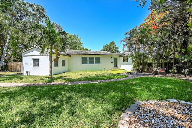 back of property featuring a yard, stucco siding, a tiled roof, and fence