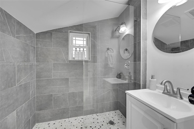 bathroom with a tile shower, visible vents, vaulted ceiling, and vanity
