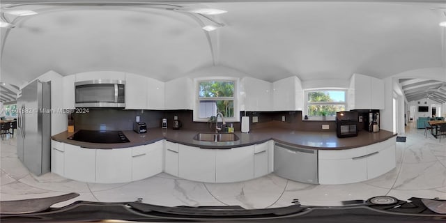 kitchen with a sink, marble finish floor, dark countertops, appliances with stainless steel finishes, and lofted ceiling