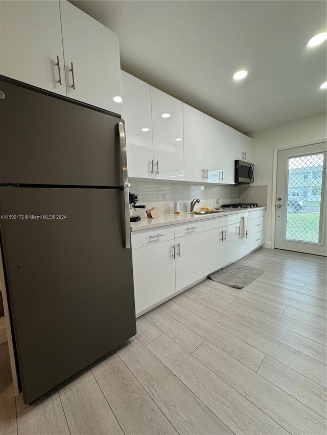 kitchen with backsplash, sink, appliances with stainless steel finishes, light hardwood / wood-style floors, and white cabinetry