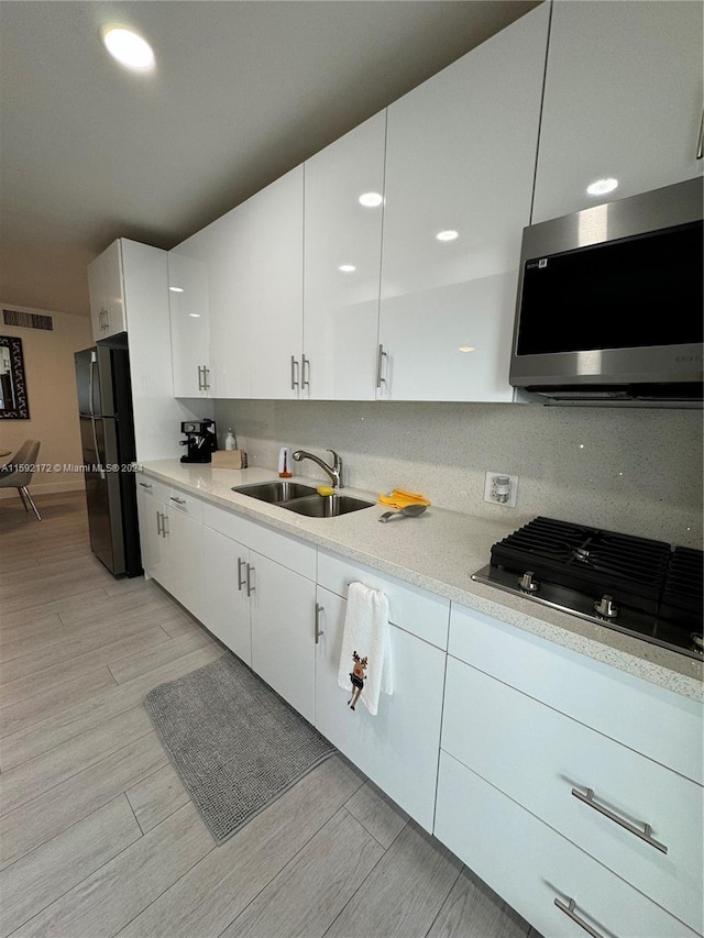 kitchen featuring backsplash, black gas cooktop, white cabinets, sink, and fridge