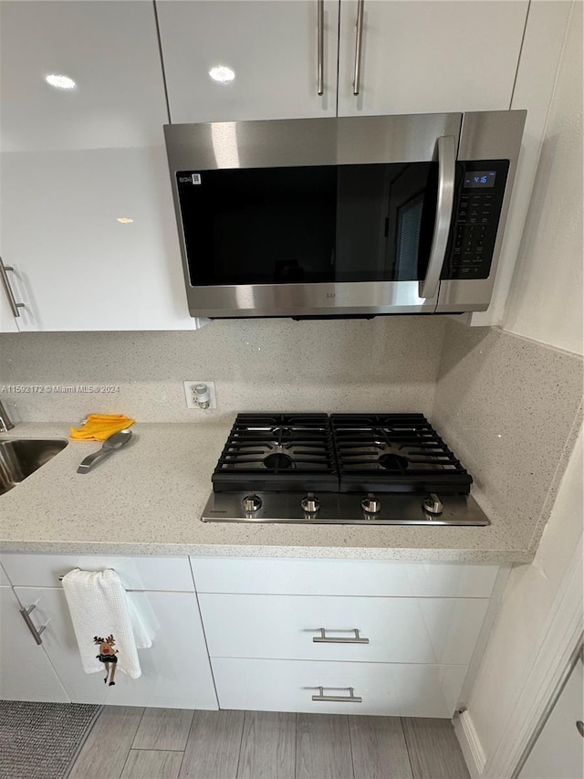 kitchen featuring light stone countertops, black gas cooktop, white cabinetry, and sink