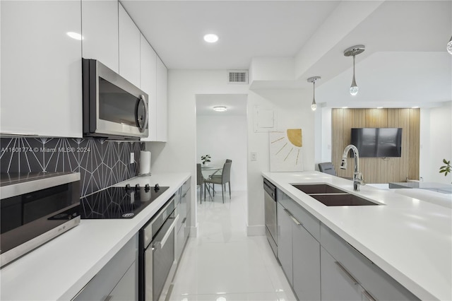 kitchen with sink, white cabinetry, appliances with stainless steel finishes, pendant lighting, and backsplash