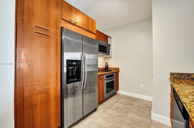 kitchen with dark stone countertops, light tile patterned floors, and stainless steel appliances