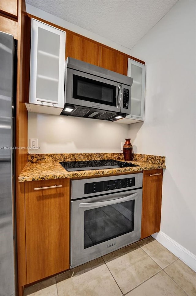 kitchen featuring stainless steel appliances, light tile patterned floors, stone counters, and a textured ceiling