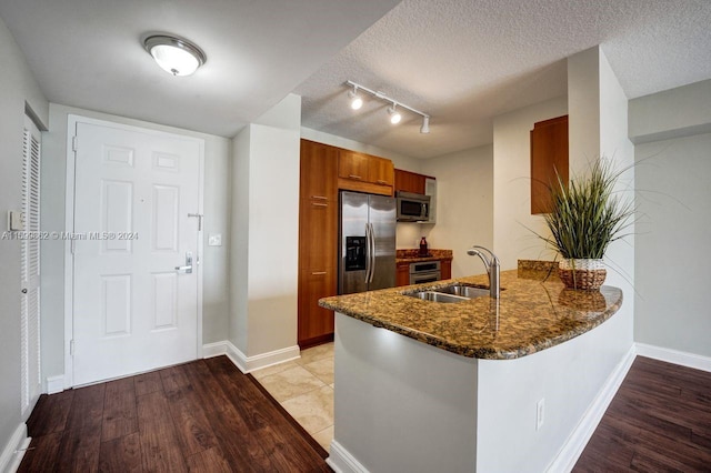 kitchen featuring appliances with stainless steel finishes, sink, kitchen peninsula, a textured ceiling, and light wood-type flooring