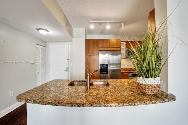 kitchen with dark stone countertops, stainless steel fridge with ice dispenser, sink, and a textured ceiling