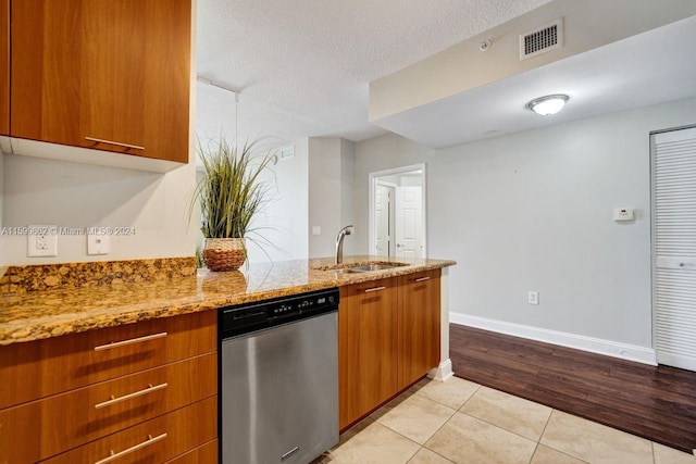 kitchen featuring dishwasher, sink, light tile patterned floors, light stone countertops, and a textured ceiling