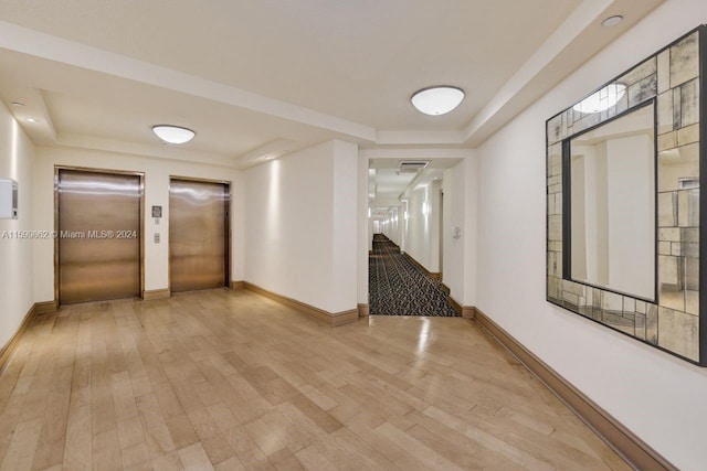 hall with a tray ceiling, light hardwood / wood-style floors, and elevator