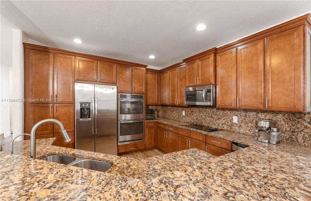 kitchen featuring light stone counters, stainless steel appliances, sink, and backsplash