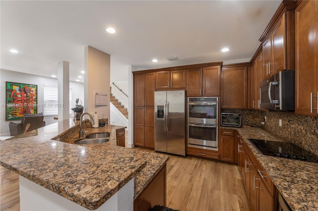 kitchen with sink, dark stone countertops, backsplash, light hardwood / wood-style floors, and stainless steel appliances