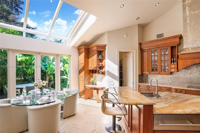 kitchen with sink, backsplash, light stone counters, a skylight, and a kitchen island with sink