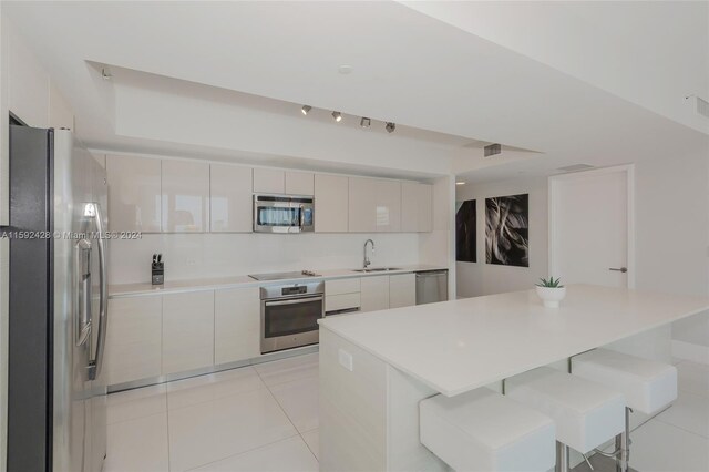 kitchen with modern cabinets, a breakfast bar area, appliances with stainless steel finishes, a sink, and light tile patterned flooring