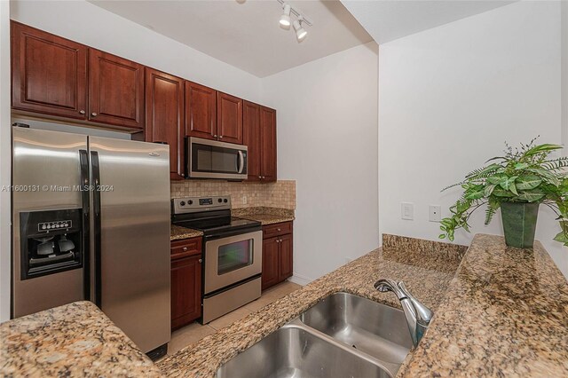 kitchen with light tile patterned floors, stainless steel appliances, sink, track lighting, and decorative backsplash