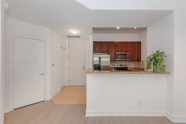 kitchen with tasteful backsplash, kitchen peninsula, light stone countertops, appliances with stainless steel finishes, and light hardwood / wood-style floors