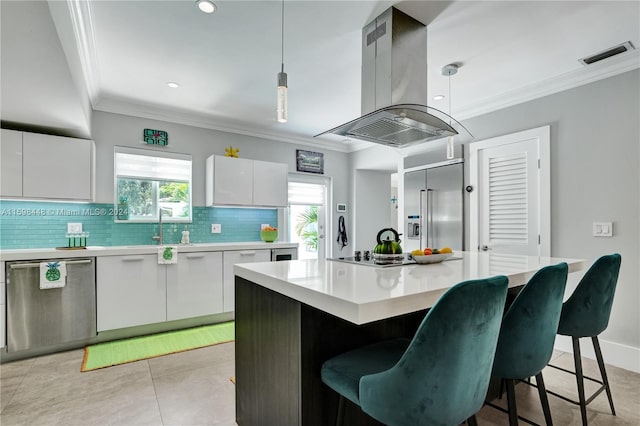 kitchen with appliances with stainless steel finishes, island range hood, a kitchen island, white cabinetry, and hanging light fixtures