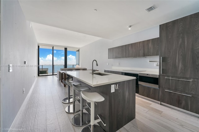 kitchen featuring a breakfast bar, a water view, sink, an island with sink, and light hardwood / wood-style floors