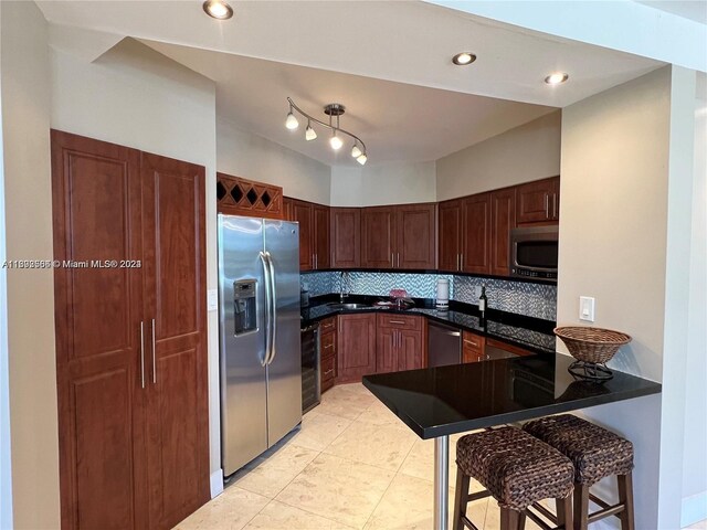 kitchen featuring light tile flooring, kitchen peninsula, backsplash, rail lighting, and appliances with stainless steel finishes