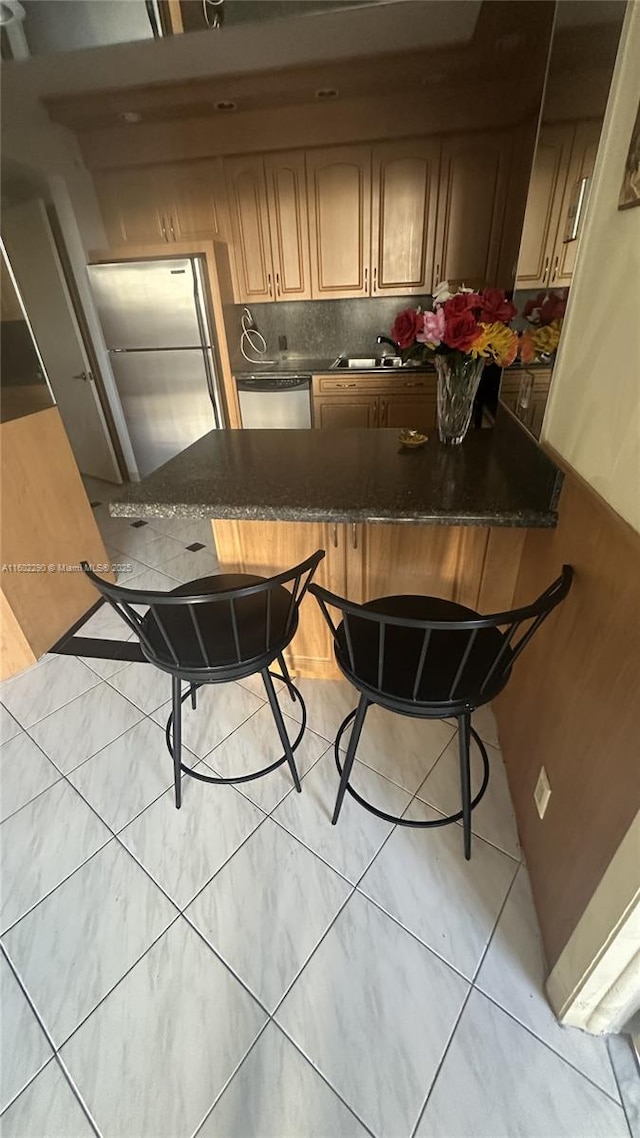 kitchen with dark stone countertops, a breakfast bar area, stainless steel appliances, kitchen peninsula, and sink