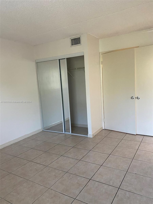 unfurnished bedroom featuring a closet, light tile patterned flooring, and a textured ceiling