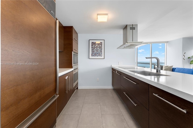 kitchen with dark brown cabinets, island range hood, black electric cooktop, light tile floors, and sink