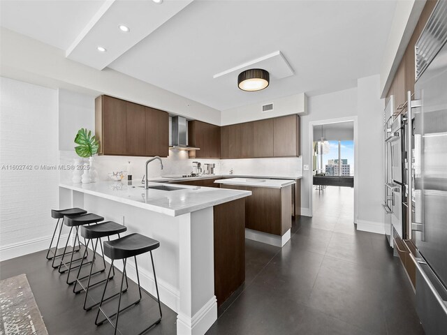 kitchen featuring sink, a breakfast bar area, kitchen peninsula, wall chimney range hood, and backsplash