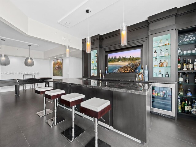 bar with wine cooler, hanging light fixtures, and dark stone countertops