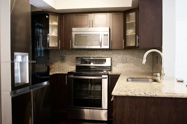 kitchen with dark brown cabinetry, tasteful backsplash, light stone countertops, appliances with stainless steel finishes, and sink