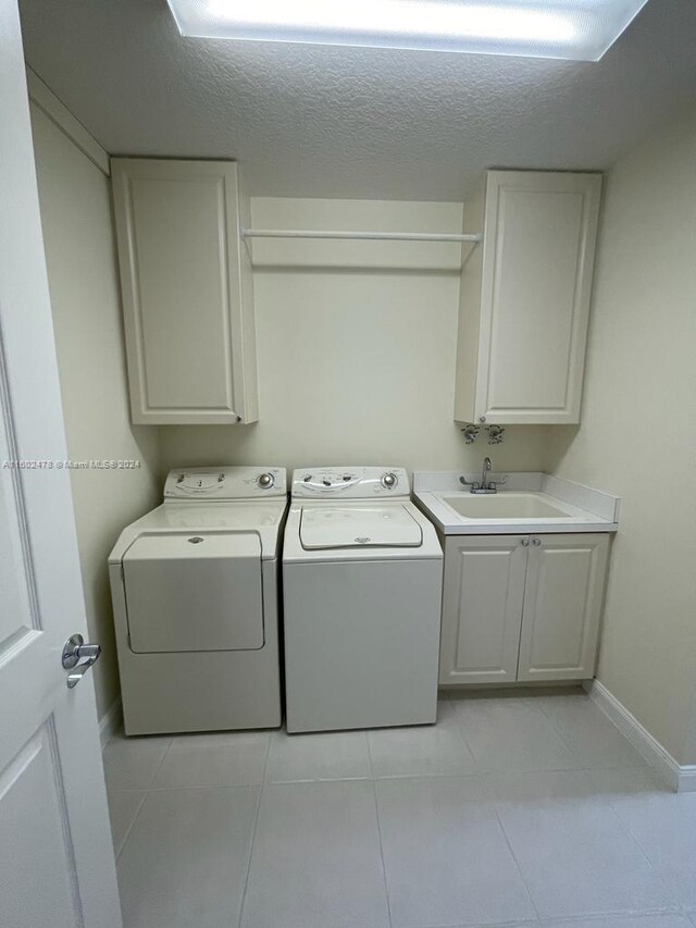 laundry area featuring cabinets, independent washer and dryer, a textured ceiling, sink, and light tile patterned flooring