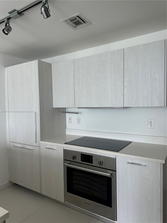 kitchen with light brown cabinetry, stainless steel oven, track lighting, and black electric cooktop