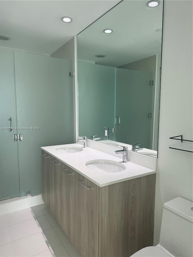 bathroom with tile patterned floors, dual vanity, toilet, and a shower with door