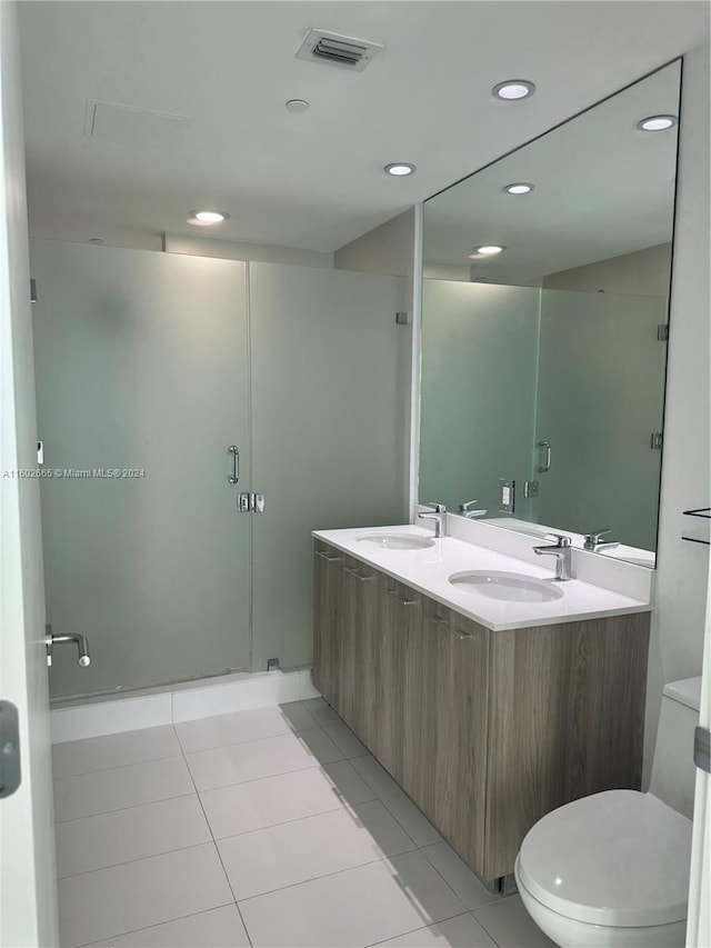 bathroom with a shower with shower door, double vanity, tile patterned flooring, and toilet