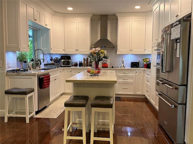 kitchen featuring backsplash, wall chimney range hood, a kitchen bar, and appliances with stainless steel finishes