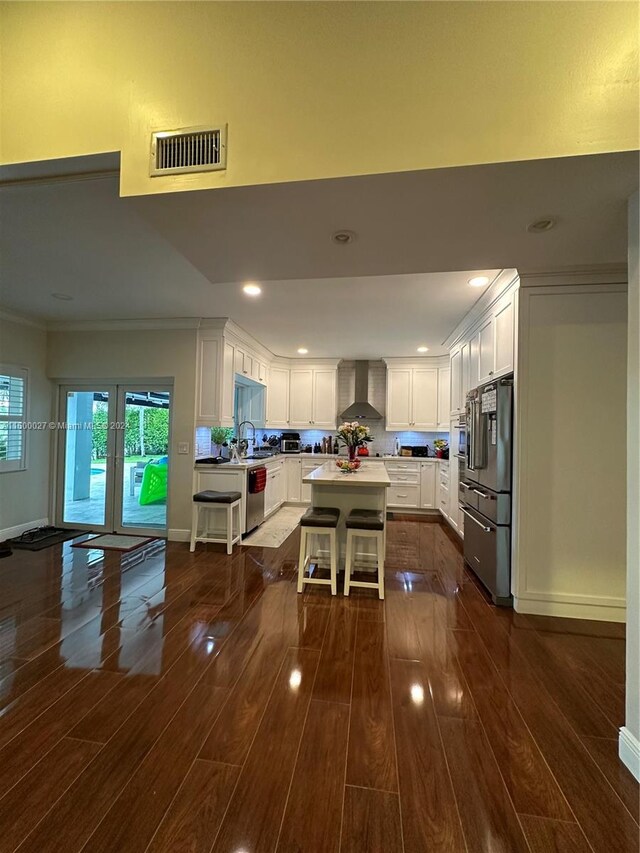 kitchen featuring white cabinets, dark wood-type flooring, a kitchen island, and wall chimney exhaust hood