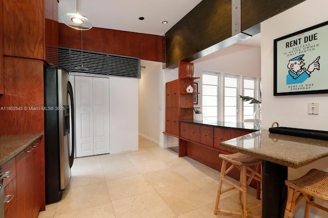kitchen with a kitchen breakfast bar, stainless steel fridge, modern cabinets, brown cabinetry, and dark stone countertops