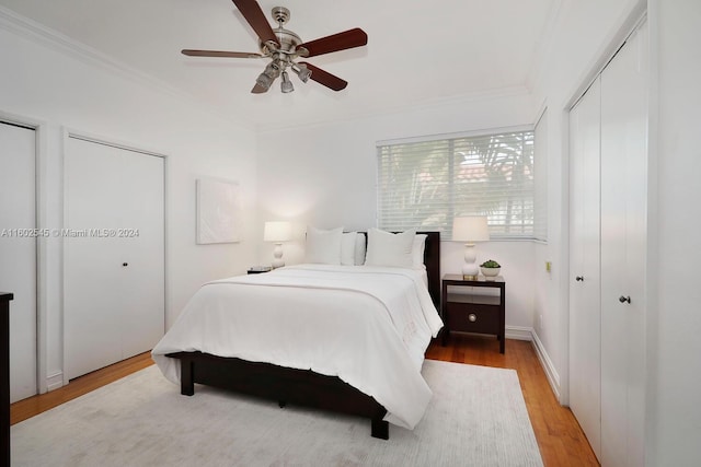 bedroom with multiple closets, light hardwood / wood-style floors, ceiling fan, and crown molding