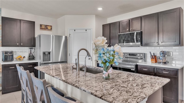 kitchen with a center island with sink, light tile patterned floors, appliances with stainless steel finishes, and decorative backsplash