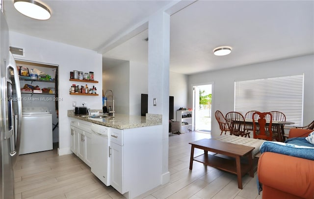 kitchen featuring washer / dryer, sink, light stone counters, dishwasher, and white cabinets