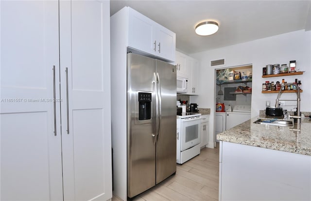 kitchen with sink, white cabinetry, white appliances, light stone countertops, and washing machine and dryer