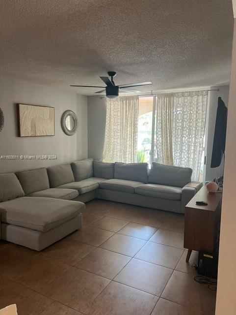 living room with ceiling fan, tile patterned flooring, and a textured ceiling