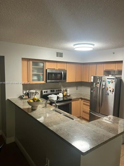 kitchen featuring sink, light stone countertops, a textured ceiling, appliances with stainless steel finishes, and kitchen peninsula