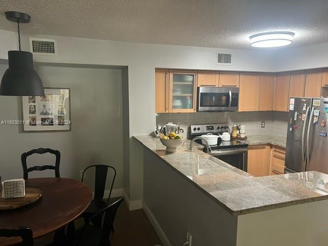 kitchen with kitchen peninsula, light stone countertops, stainless steel appliances, and a textured ceiling