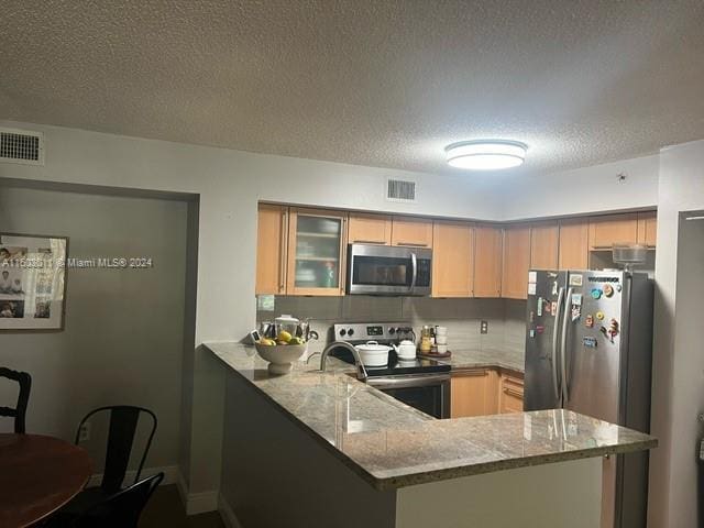 kitchen featuring kitchen peninsula, a textured ceiling, stainless steel appliances, and light stone counters