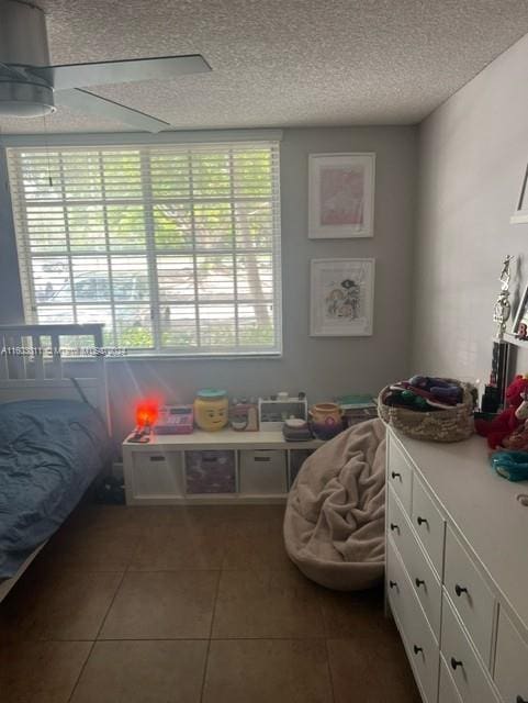 bedroom featuring dark tile patterned flooring, ceiling fan, a textured ceiling, and multiple windows