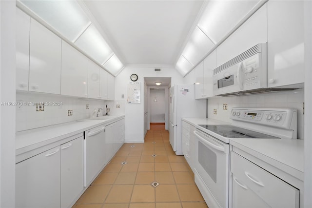 kitchen with white appliances, sink, vaulted ceiling, light tile patterned floors, and white cabinetry