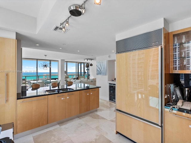 kitchen featuring sink, beverage cooler, paneled built in refrigerator, dark stone counters, and a water view