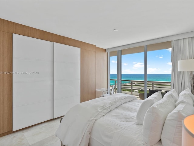 bedroom with wood walls, floor to ceiling windows, access to outside, a water view, and a beach view