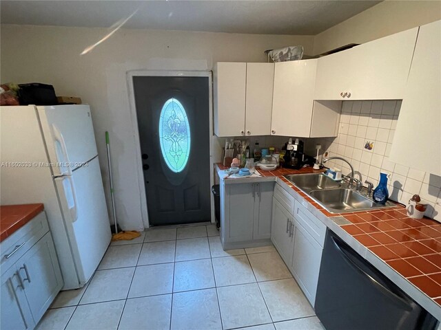 kitchen with tile countertops, backsplash, white cabinets, sink, and white fridge