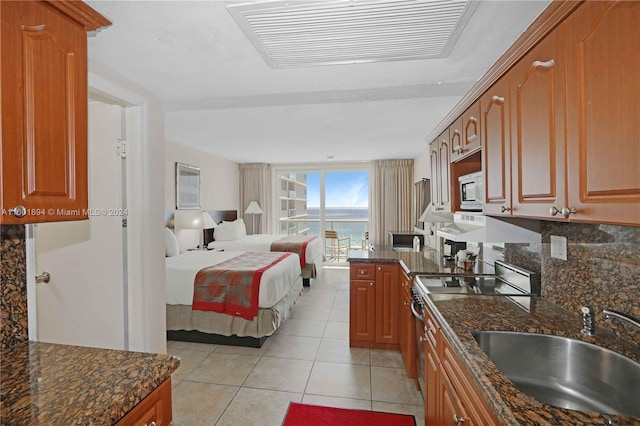 kitchen with tasteful backsplash, sink, stainless steel range with electric cooktop, light tile patterned floors, and dark stone countertops