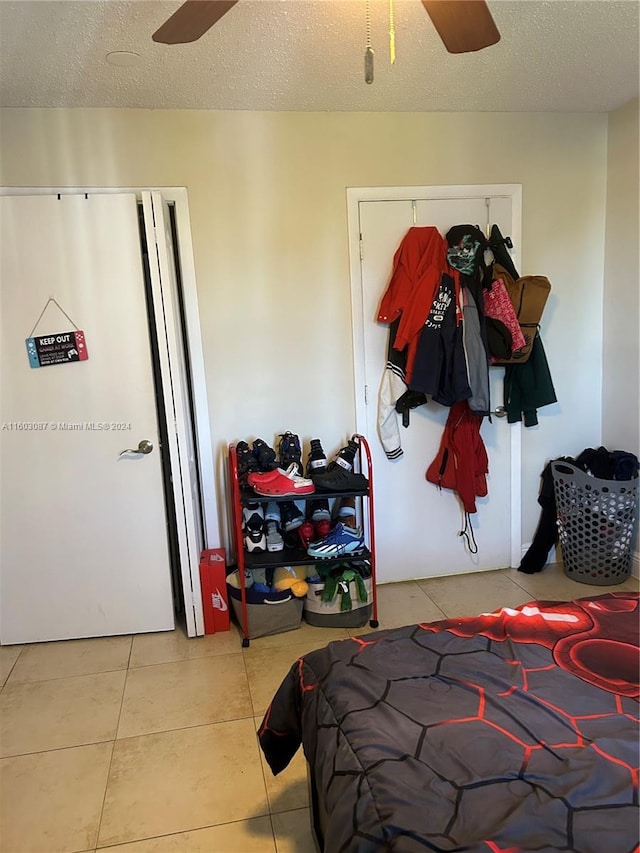 bedroom featuring a textured ceiling, a closet, light tile patterned floors, and ceiling fan